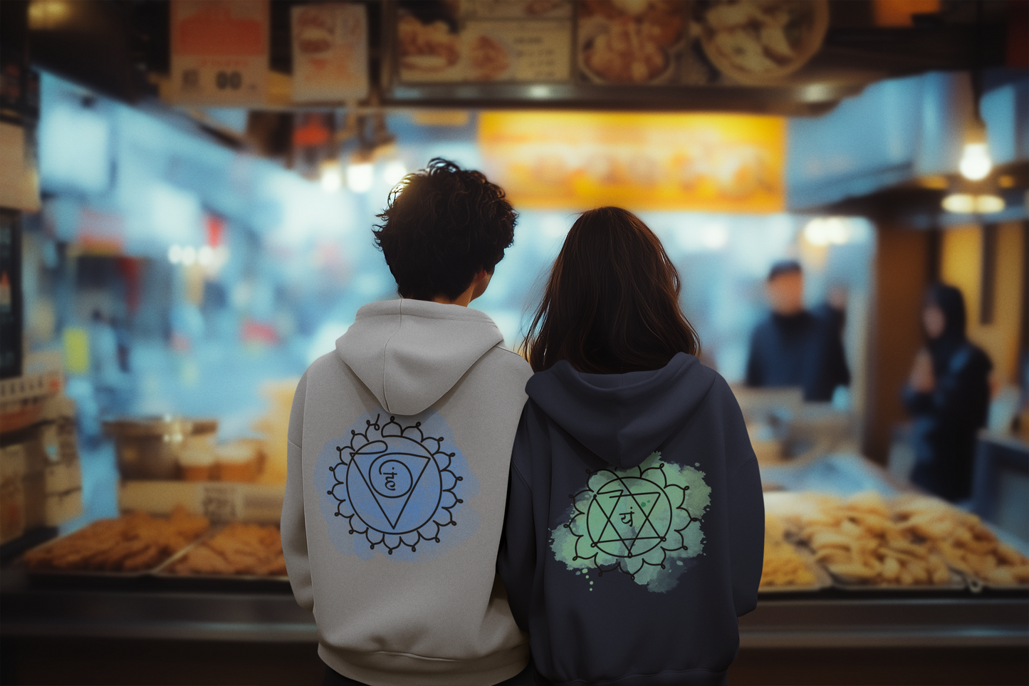 Man and woman sitting back-to-back at a vibrant Asian market wearing comfortable gray and black chakra hoodies featuring Anahata and Vishuddha designs. Perfect for a unisex look from Inkasis.